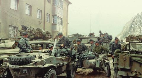 Colourised period photograph: German troops with Schwimmwagen, motorcycle and vehicles in a snowy mountain town