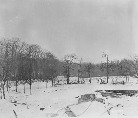 Period photograph: small figures running across a snow-covered slope with rows of obstacles, bare trees behind