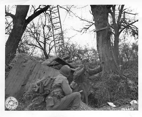 Period photograph: a man emerging from a dugout under a tree, a soldier with a rifle beside it, a ladder against the tree