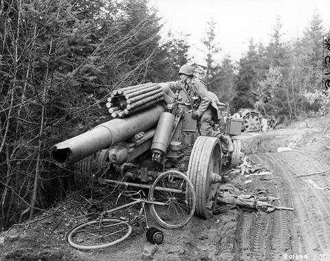 Period photograph: a soldier standing on a wrecked artillery piece on a forest track, a bicycle and debris in front