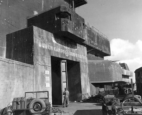 Period photograph: two soldiers at a huge concrete entrance with painted German lettering, a jeep in front