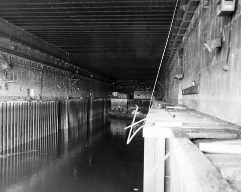 Period photograph: an empty water-filled dock running into a dark concrete hall