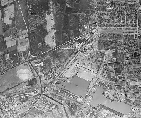Period photograph: aerial view of docks and a large rectangular bunker beside a river, factory buildings to the right