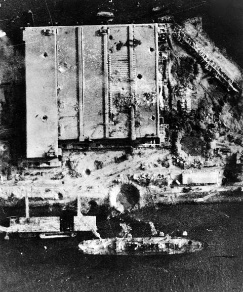 Period photograph: aerial view of a large bunker beside a harbour, the ground around it covered with bomb craters