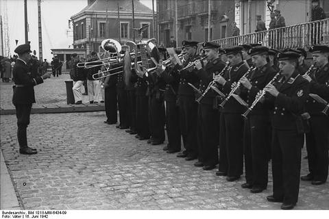 Period photograph: a uniformed band with brass instruments playing on a quayside