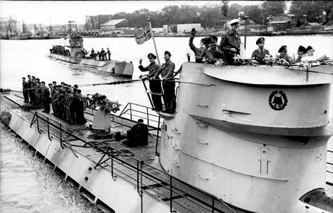 Period photograph: two submarines under way in a harbour, crews on deck and conning towers waving
