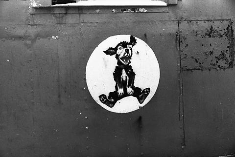 Period photograph: close view of a painted circular emblem with a cartoon figure on a steel surface