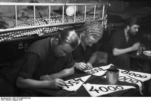 Period photograph: sailors inside a submarine painting numbers on small pennants