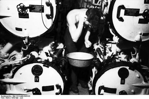 Period photograph: a sailor washing at a basin in a cramped compartment, torpedo tubes behind