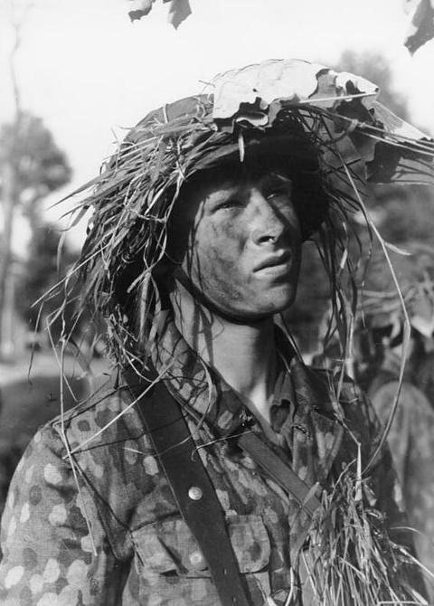 Period photograph: portrait of a young soldier in a camouflage smock, his helmet covered with foliage