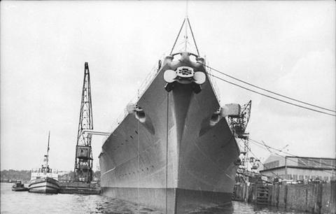 Period photograph: the bow of a large battleship moored at a quay, seen head-on