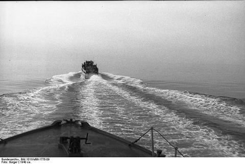 Period photograph: a motor torpedo boat far ahead at sea, seen over the bow of another, a broad white wake between them