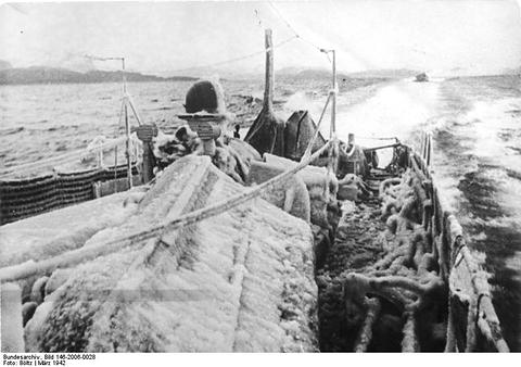 Period photograph: a sailor in heavy foul-weather clothing on the ice-covered deck of a boat under way
