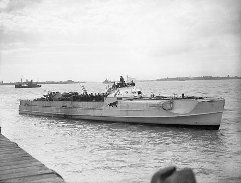 Period photograph: a motor torpedo boat with a small white flag and a painted panther emblem, men on deck, lying off a wooden jetty