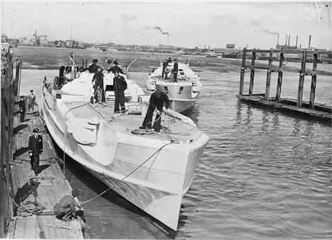 Period photograph: two motor torpedo boats with crews on deck mooring beside a wooden jetty