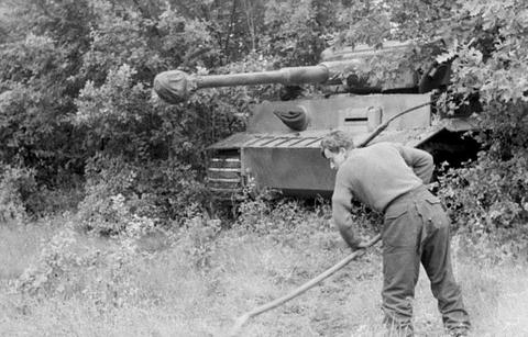 Period photograph: a soldier with a broom in front of a Tiger tank hidden under branches