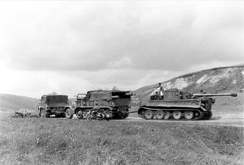 Period photograph: a truck and two large half-tracks towing a tank along a road across open country