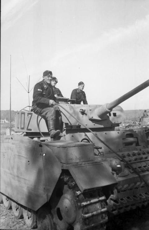 Period photograph: three soldiers on a tank with armour skirts, seen from the front