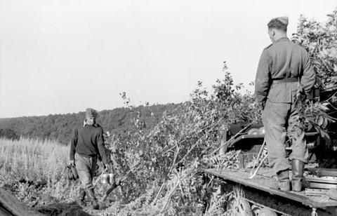 Period photograph: soldiers piling branches over a vehicle at the edge of a field