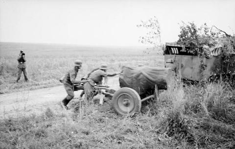Period photograph: soldiers pushing a wheeled launcher along a track past a camouflaged vehicle