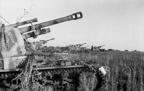 Period photograph: a line of self-propelled guns covered with branches in a field