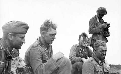 Period photograph: a group of weary soldiers sitting together, one standing with a camera