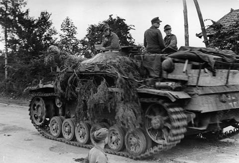 Period photograph: an assault gun covered in branches, its crew on top