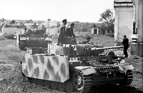 Period photograph: a tank with a mottled camouflage pattern beside village houses