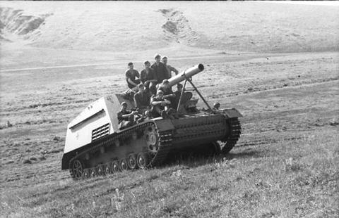 Period photograph: a self-propelled gun with soldiers on top driving up a grassy hillside