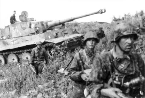 Period photograph: soldiers in camouflaged helmets in front of a Tiger tank in high grass