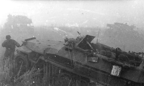 Period photograph: a half-track and soldiers moving through thick smoke
