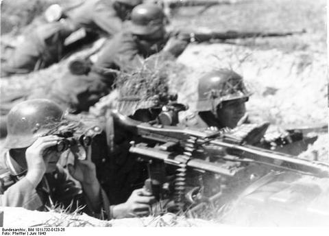 Period photograph: soldiers lying behind a machine gun, one looking through binoculars