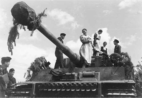 Period photograph: women and men in folk dress standing on a Tiger tank