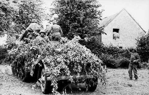 Period photograph: soldiers on a half-track so thickly covered with foliage that only its tracks show