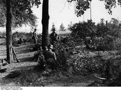 Period photograph: armed men in helmets crouching among trees and bushes