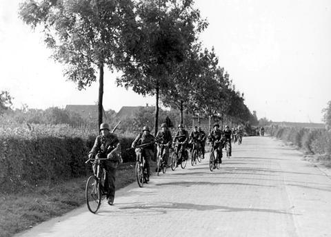 Period photograph: soldiers riding bicycles in file along a tree-lined road