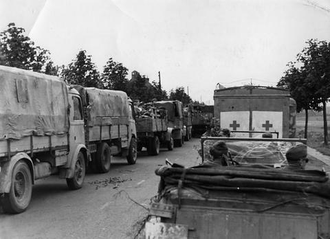 Period photograph: a column of parked lorries and an ambulance on a tree-lined street