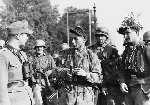 Period photograph: a group of soldiers in smocks and helmets, some with leaves on their headgear