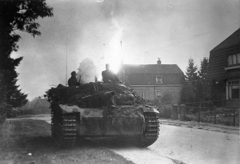 Period photograph: an armoured vehicle on a street with a bright fire behind houses