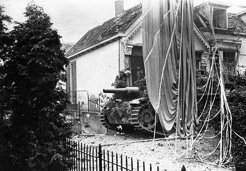 Period photograph: an armoured vehicle beside a house, a parachute hanging in front