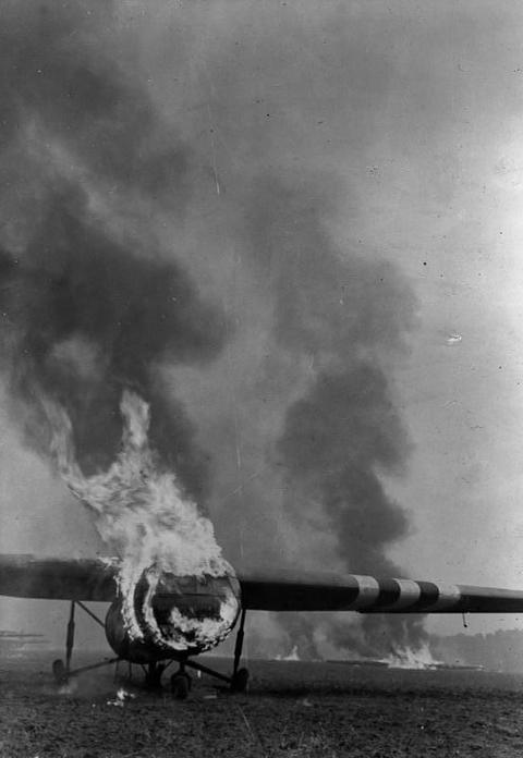 Period photograph: a glider on fire on a field, a column of black smoke above