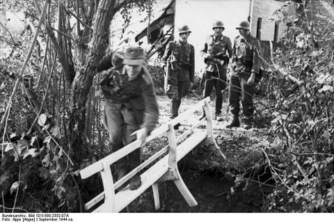 Period photograph: soldiers crossing a narrow bridge of planks among trees