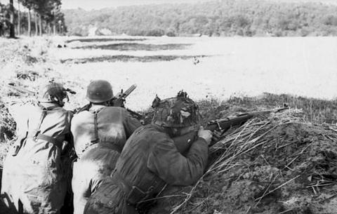 Period photograph: three soldiers lying behind a bank of earth, aiming across a field