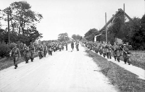 Period photograph: two files of soldiers walking down a straight village road