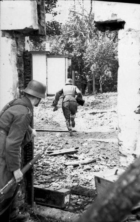 Period photograph: a soldier running across rubble between the walls of houses