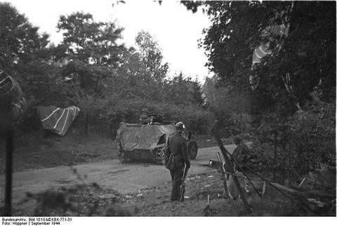 Period photograph: a soldier on a road in woodland, a half-track behind him