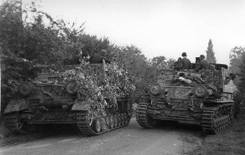 Period photograph: two tracked vehicles covered with branches on a lane