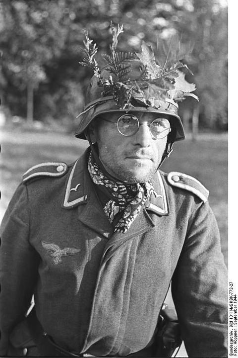 Period photograph: a man in glasses wearing a helmet decorated with leaves