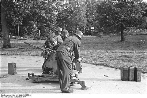 Period photograph: soldiers at a light anti-aircraft gun on a path, ammunition boxes nearby