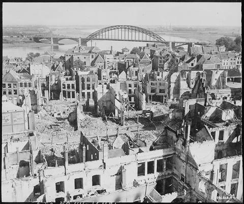 Period photograph: roofless buildings in the foreground, an arched bridge over a river beyond